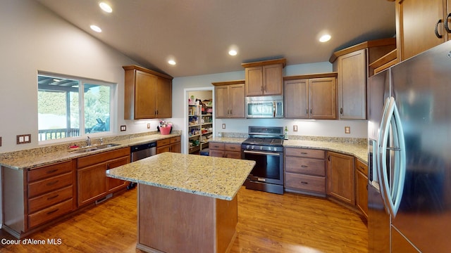 kitchen with light stone countertops, appliances with stainless steel finishes, a sink, a kitchen island, and vaulted ceiling