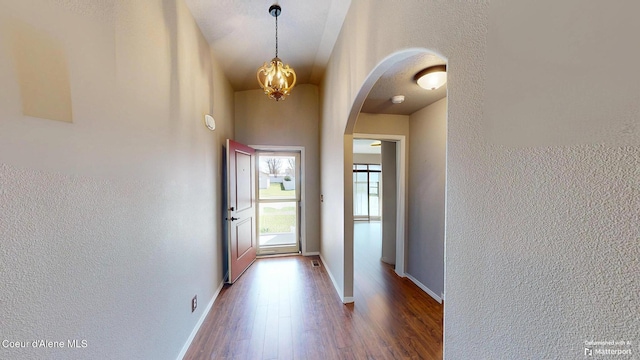 hall featuring arched walkways, a textured wall, and wood finished floors