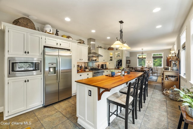 1201 Paradise Valley Rd, Bonners Ferry, ID 83805 - kitchen with appliances with stainless steel finishes, wall chimney range hood, wooden counters, white cabinets, and a breakfast bar