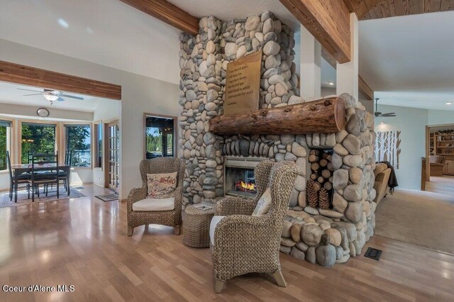 living room featuring ceiling fan, lofted ceiling with beams, a stone fireplace, and wood finished floors