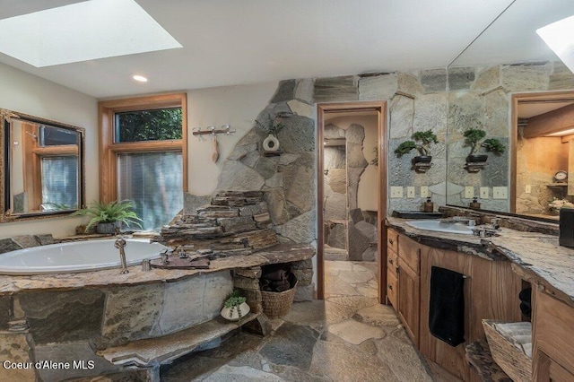 full bathroom featuring a skylight, vanity, stone flooring, and a bath