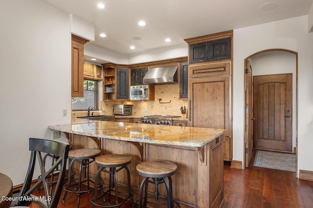 6012 W Quartzite Ln, Coeur Dalene, ID 83814 - kitchen with wall chimney exhaust hood, stainless steel microwave, dark wood finished floors, a sink, and a peninsula