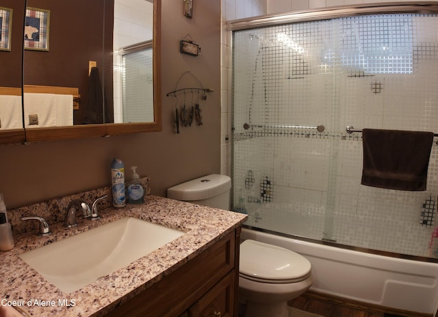 bathroom with bath / shower combo with glass door, vanity, and toilet