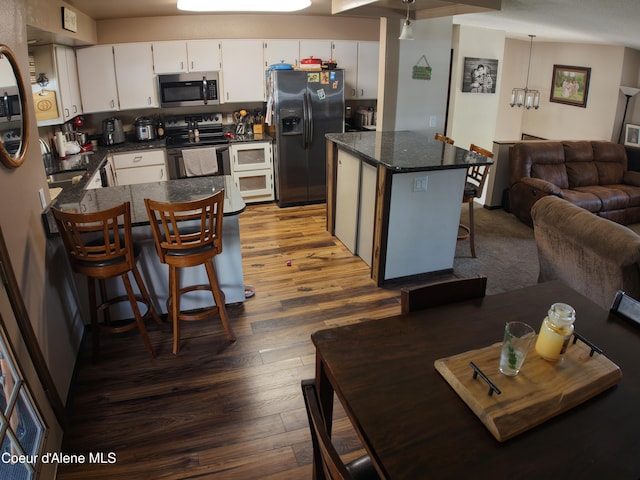 kitchen with a breakfast bar area, range with electric cooktop, stainless steel microwave, refrigerator with ice dispenser, and dark wood-style floors