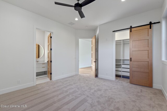 unfurnished bedroom featuring carpet floors, visible vents, baseboards, a barn door, and a spacious closet