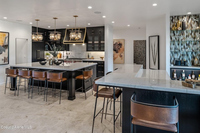 17056 S Lazurite Dr, Coeur Dalene, ID 83814 - kitchen featuring decorative backsplash, a kitchen breakfast bar, ventilation hood, dark cabinetry, and recessed lighting