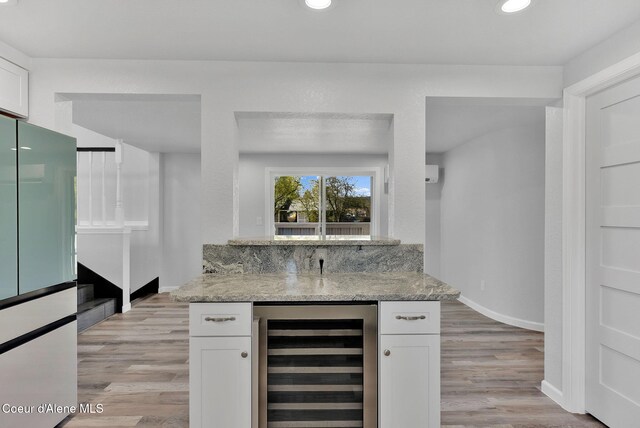 bar featuring wine cooler, bar, baseboards, and light wood-type flooring