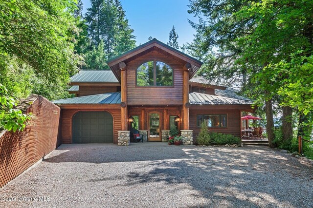 rustic home featuring an attached garage, covered porch, gravel driveway, and metal roof