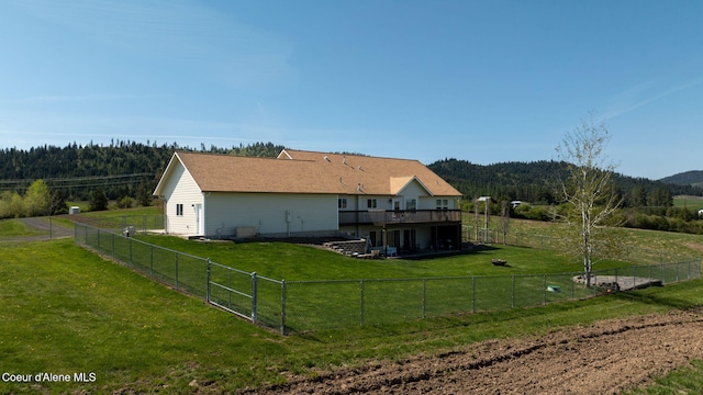 back of property with a yard, a forest view, a wooden deck, and a fenced backyard