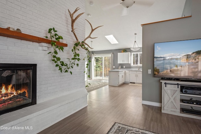 interior space with ceiling fan, wood finished floors, a skylight, and a brick fireplace