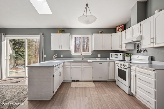 kitchen with under cabinet range hood, white appliances, a sink, white cabinets, and a skylight