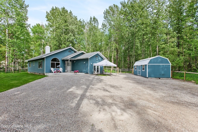 view of front of property featuring fence, a chimney, an outdoor structure, a front yard, and driveway