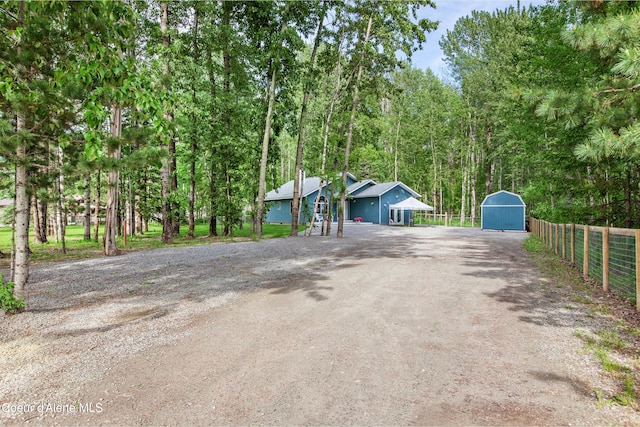 exterior space with fence, dirt driveway, an outdoor structure, and a storage shed