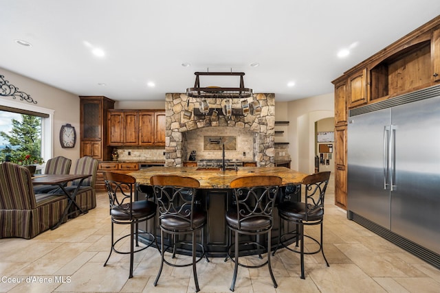5969 W Highland Dr, Coeur Dalene, ID 83814 - kitchen with decorative backsplash, stone finish flooring, arched walkways, a large island with sink, and stainless steel built in refrigerator