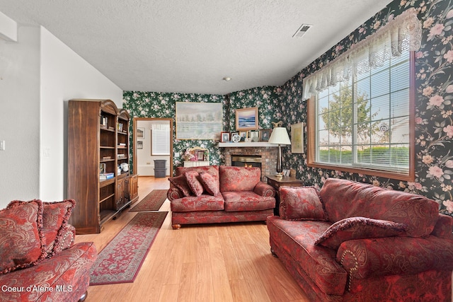 404 W 18th Ave, Post Falls, ID 83854 - living area with wallpapered walls, light wood-type flooring, visible vents, a textured ceiling, and a warm lit fireplace