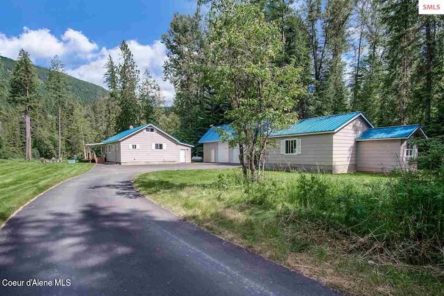 ranch-style house featuring a detached garage, a front yard, a forest view, an outdoor structure, and metal roof