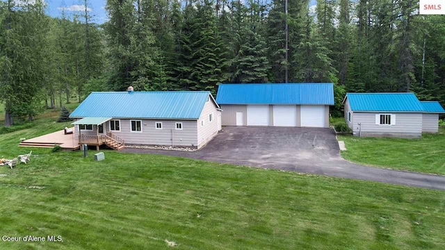 view of front facade featuring a garage, a front lawn, a deck, metal roof, and an outbuilding