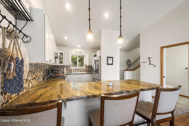 19820 S Alcan Rd, Coeur Dalene, ID 83814 - kitchen featuring stainless steel refrigerator with ice dispenser, a peninsula, backsplash, white cabinetry, and a breakfast bar