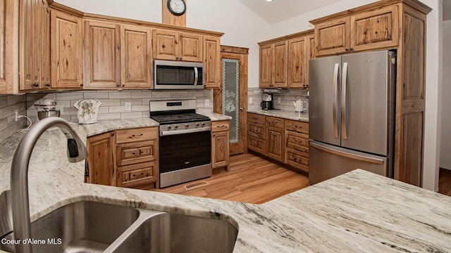 kitchen featuring backsplash, light wood-type flooring, a sink, lofted ceiling, and stainless steel appliances