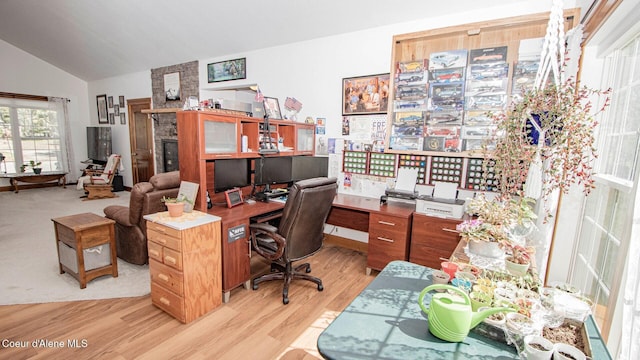 home office featuring light wood-style floors, lofted ceiling, and a stone fireplace