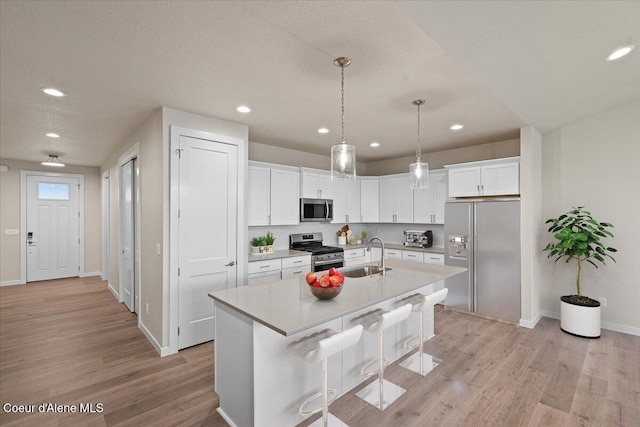 kitchen featuring a kitchen island with sink, appliances with stainless steel finishes, light wood-type flooring, a sink, and light countertops