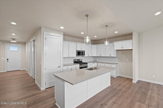 kitchen featuring appliances with stainless steel finishes, a sink, light wood-style flooring, baseboards, and tasteful backsplash