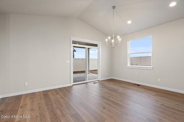 empty room featuring an inviting chandelier, lofted ceiling, wood finished floors, and visible vents