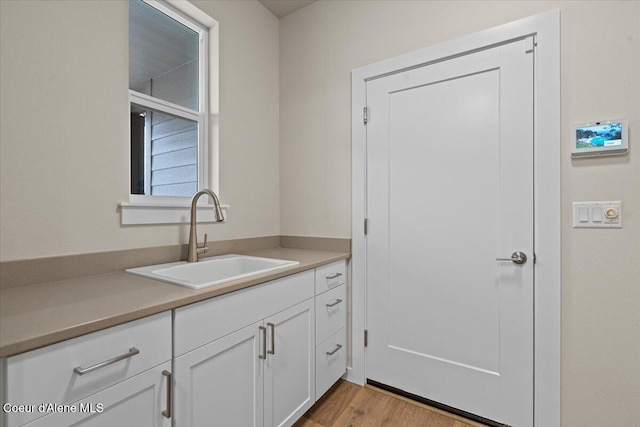 interior space with a sink, light countertops, white cabinetry, and wood finished floors