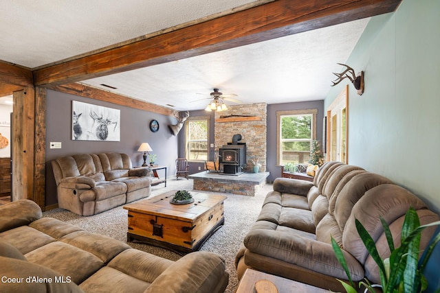 carpeted living area featuring ceiling fan, a wood stove, a textured ceiling, beamed ceiling, and visible vents