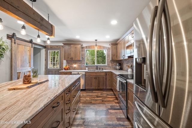 kitchen with pendant lighting, a barn door, tasteful backsplash, dark wood finished floors, and stainless steel appliances