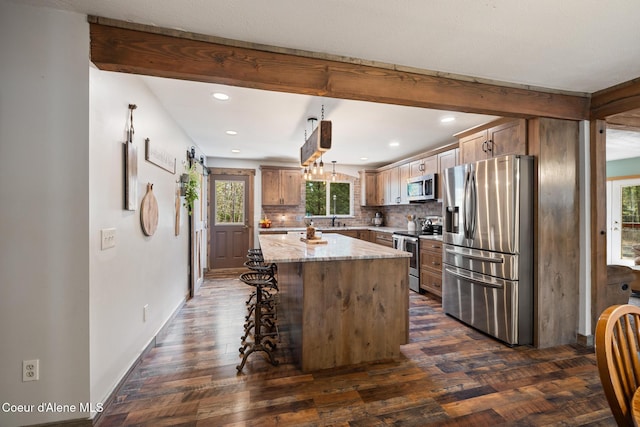 kitchen with light stone counters, a center island, stainless steel appliances, decorative backsplash, and dark wood-style floors
