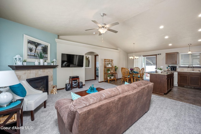 carpeted living room with a sink, arched walkways, ceiling fan with notable chandelier, a tile fireplace, and vaulted ceiling