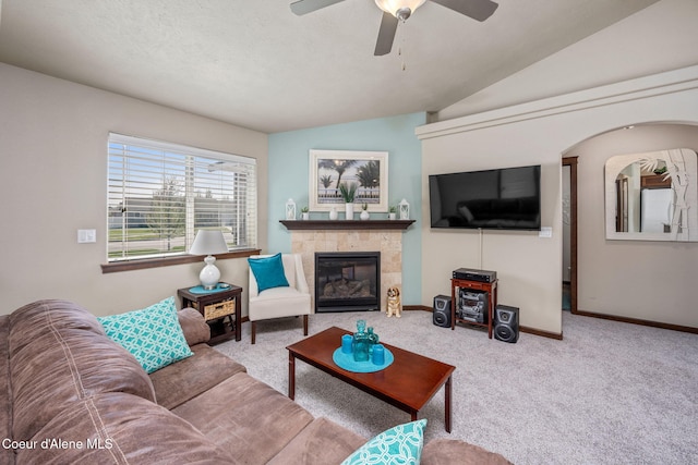 carpeted living room featuring a tiled fireplace, baseboards, ceiling fan, and lofted ceiling