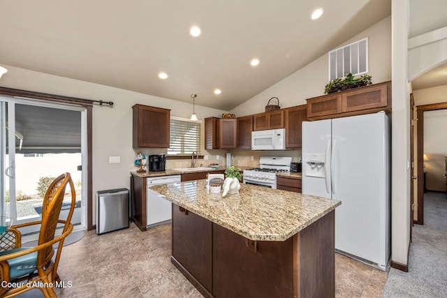 kitchen with a kitchen island, visible vents, light stone countertops, a sink, and white appliances