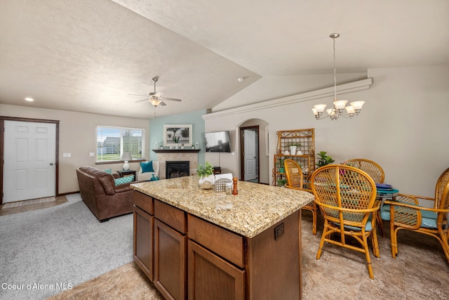 kitchen with a fireplace, ceiling fan with notable chandelier, decorative light fixtures, a kitchen island, and vaulted ceiling
