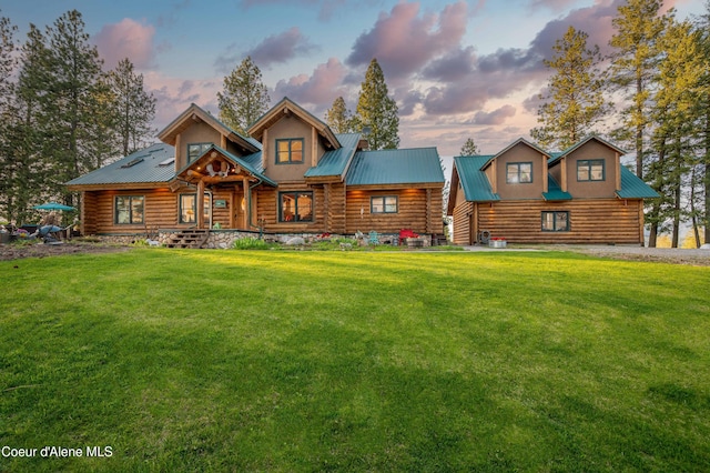 back of property at dusk with a lawn, covered porch, log siding, and metal roof