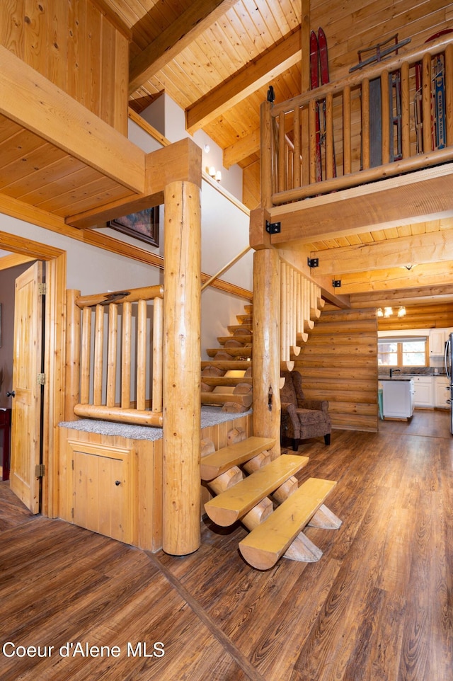 staircase with beam ceiling, wood finished floors, wooden ceiling, a high ceiling, and rustic walls