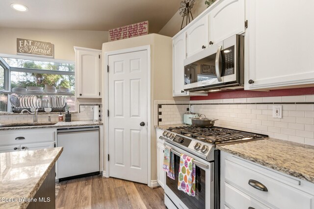 kitchen with tasteful backsplash, a sink, light stone counters, white cabinets, and stainless steel appliances