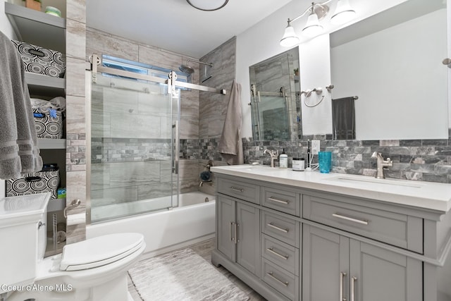 full bath with double vanity, toilet, bath / shower combo with glass door, and a sink