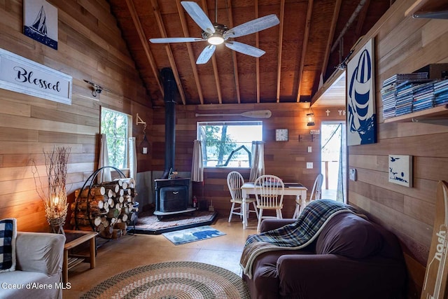 living area with wood walls, lofted ceiling, a wood stove, wooden ceiling, and a ceiling fan