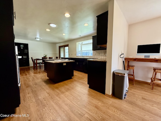 kitchen featuring a kitchen island, light wood-style floors, recessed lighting, dark cabinets, and backsplash