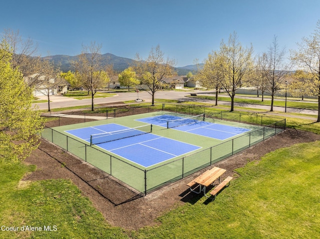 view of tennis court featuring a lawn, a mountain view, and fence