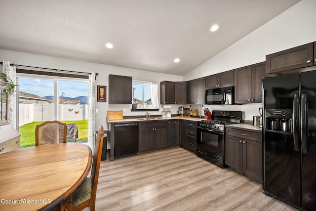 kitchen with dark brown cabinetry, a sink, light wood finished floors, lofted ceiling, and black appliances