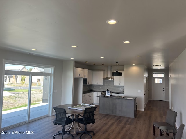 kitchen with dark countertops, dark wood finished floors, wall chimney exhaust hood, a center island, and white cabinetry