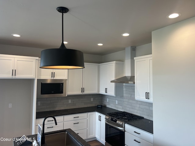 kitchen featuring wall chimney range hood, white cabinetry, dark countertops, and appliances with stainless steel finishes