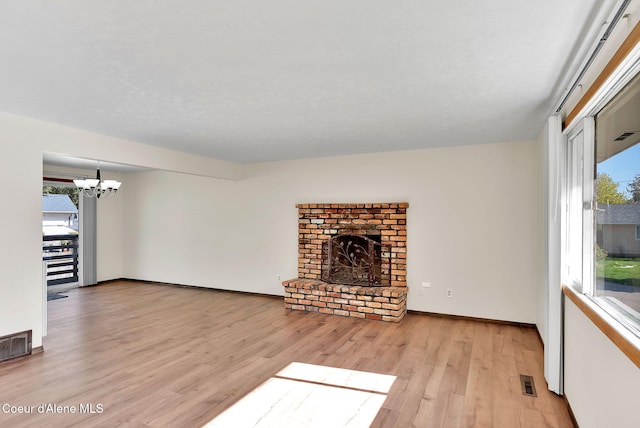 407 E Buttercup Ln, Coeur Dalene, ID 83815 - unfurnished living room with an inviting chandelier, a brick fireplace, wood finished floors, and a wealth of natural light