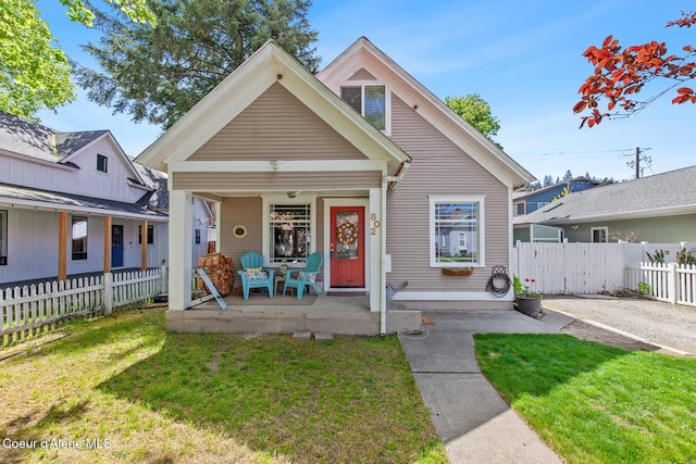 bungalow with covered porch, fence, and a front yard
