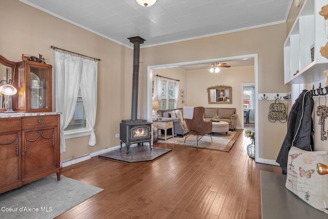 living area featuring hardwood / wood-style flooring, a wood stove, crown molding, ceiling fan, and baseboard heating