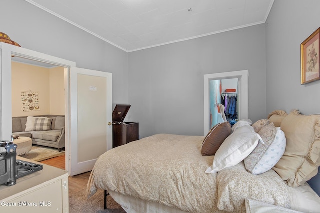 bedroom with a spacious closet, light wood-type flooring, a closet, and ornamental molding