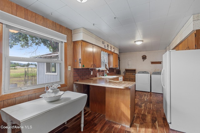 17871 N Ramsey Rd, Rathdrum, ID 83858 - kitchen with freestanding refrigerator, washer and dryer, a peninsula, dark wood-style flooring, and brown cabinets
